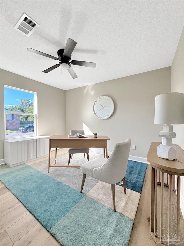 office featuring ceiling fan, light wood-type flooring, and a textured ceiling