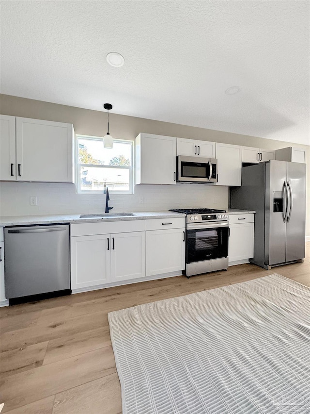 kitchen featuring white cabinets, stainless steel appliances, hanging light fixtures, and sink