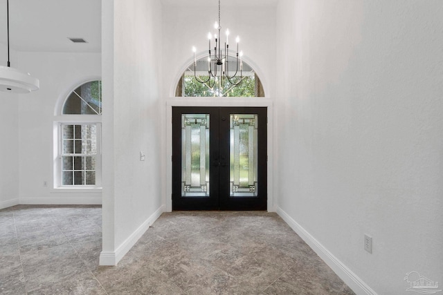 foyer entrance featuring a towering ceiling, a notable chandelier, and french doors