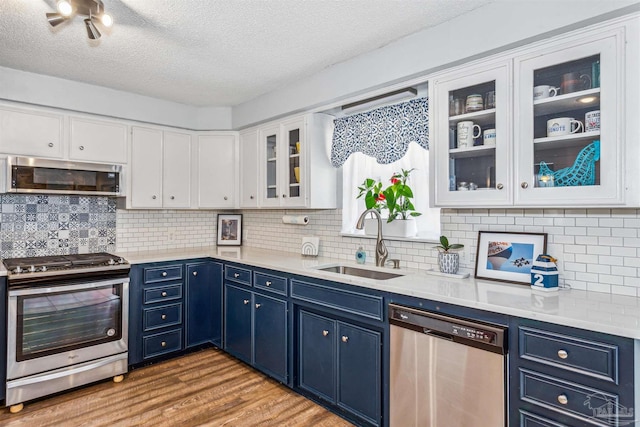 kitchen featuring white cabinets, appliances with stainless steel finishes, light wood-type flooring, blue cabinetry, and sink