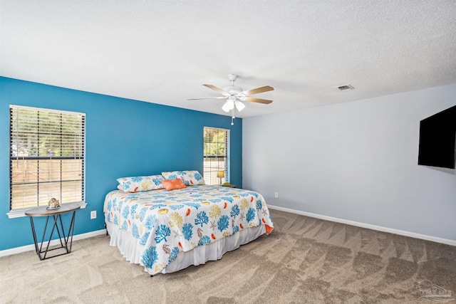 carpeted bedroom with a textured ceiling, multiple windows, and ceiling fan