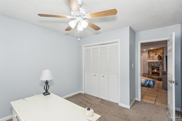 home office featuring a stone fireplace, a textured ceiling, carpet, and ceiling fan