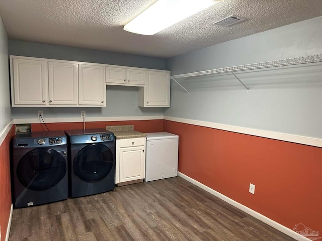 laundry area with dark wood-type flooring, a textured ceiling, separate washer and dryer, and cabinets