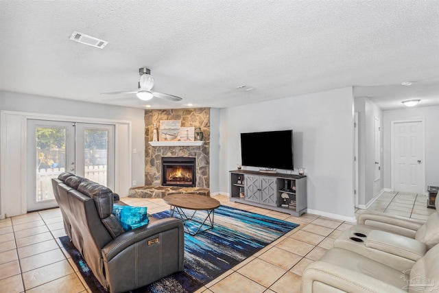 living room featuring french doors, a stone fireplace, light tile patterned floors, a textured ceiling, and ceiling fan