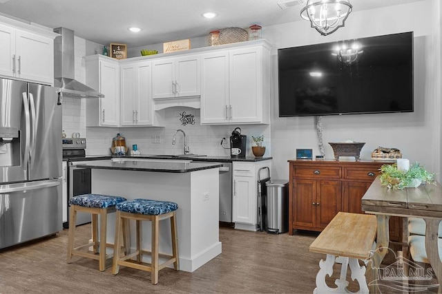 kitchen featuring appliances with stainless steel finishes, sink, a center island, wall chimney range hood, and white cabinets