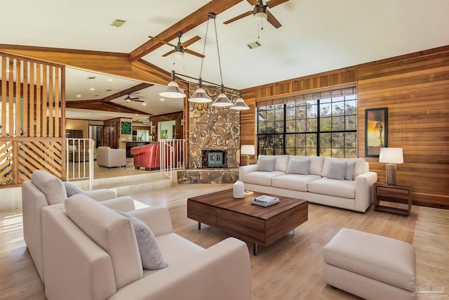 living room with vaulted ceiling with beams, light hardwood / wood-style floors, a stone fireplace, and wood walls