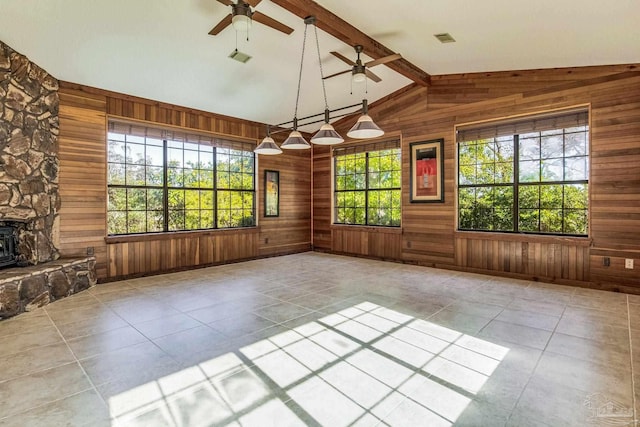 interior space with a wood stove, lofted ceiling with beams, wooden walls, ceiling fan, and light tile patterned floors