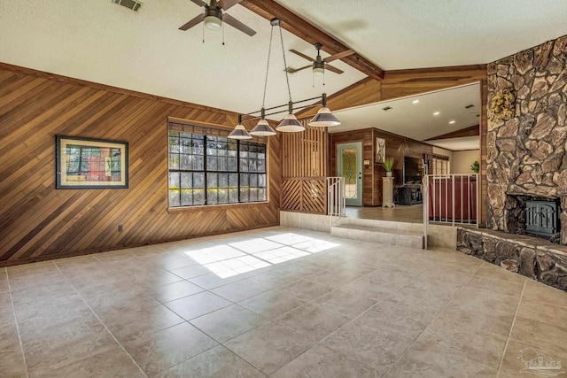 unfurnished living room with wood walls, lofted ceiling, a wood stove, ceiling fan, and a textured ceiling