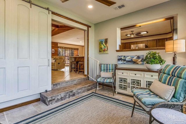 sitting room with a barn door, ceiling fan, and light tile patterned flooring