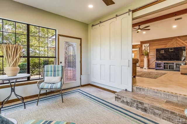 living area with a barn door, ceiling fan, and light tile patterned floors