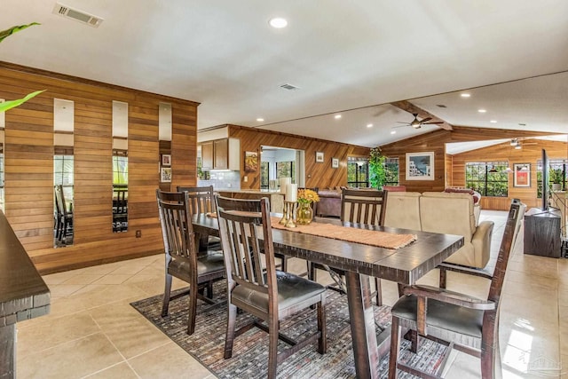 tiled dining area with wood walls, ceiling fan, and vaulted ceiling