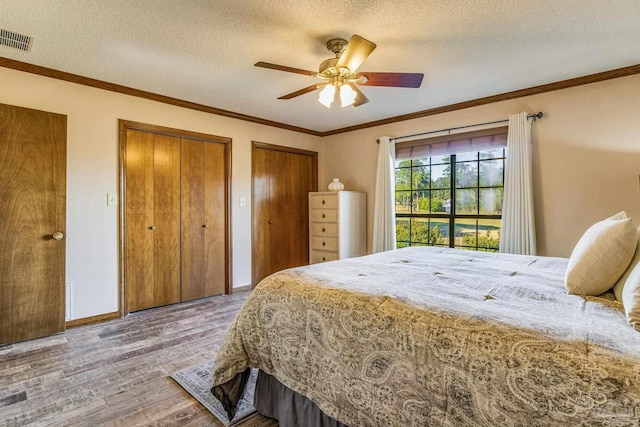 bedroom featuring multiple closets, ceiling fan, a textured ceiling, hardwood / wood-style flooring, and ornamental molding