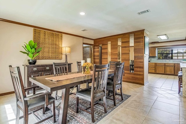 dining room with wood walls, ornamental molding, and light tile patterned floors