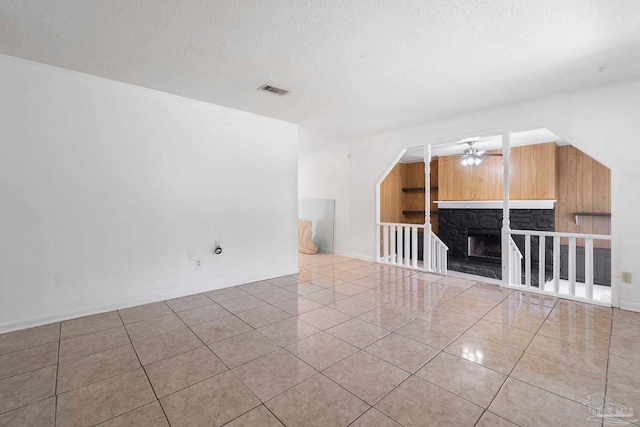401 Ronda St, Pensacola, FL 32534 - unfurnished living room featuring tile patterned flooring, ceiling fan, a textured ceiling, and a stone fireplace