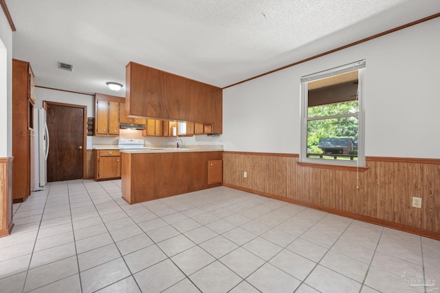 kitchen with brown cabinetry, visible vents, stove, a wainscoted wall, and a peninsula