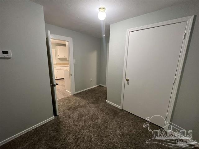 corridor featuring a textured ceiling and dark colored carpet