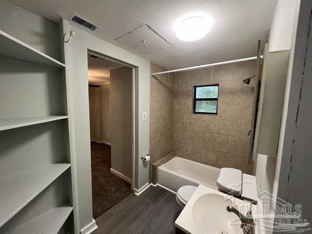 full bathroom featuring toilet, tiled shower / bath, a textured ceiling, vanity, and hardwood / wood-style floors