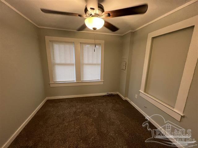 spare room with dark colored carpet, crown molding, and ceiling fan