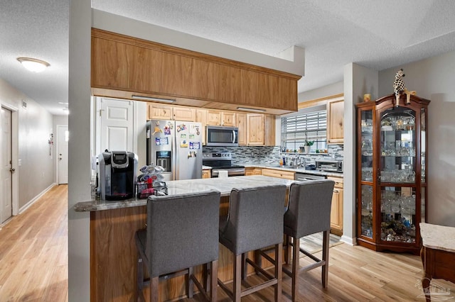 5590 Meadow Creek Pl, Gulf Breeze, FL 32563 - kitchen with stainless steel appliances, tasteful backsplash, a textured ceiling, light wood-style flooring, and a peninsula