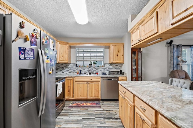 5590 Meadow Creek Pl, Gulf Breeze, FL 32563 - kitchen with appliances with stainless steel finishes, light brown cabinetry, light wood-type flooring, tasteful backsplash, and a textured ceiling