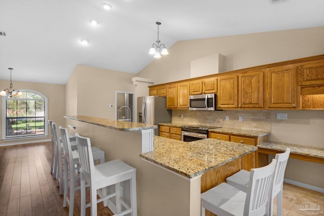 kitchen featuring light wood-type flooring, a breakfast bar area, an inviting chandelier, appliances with stainless steel finishes, and light stone countertops