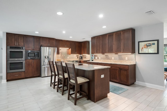 kitchen with a breakfast bar area, a kitchen island, stainless steel appliances, light stone countertops, and decorative backsplash