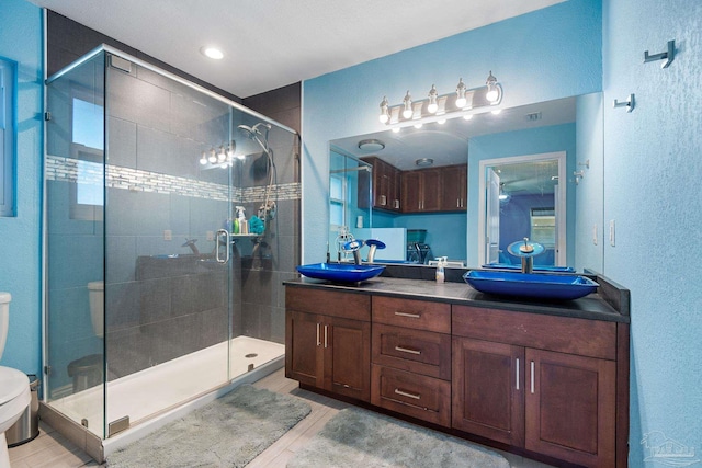 bathroom featuring a shower with shower door, tile patterned floors, double sink vanity, and toilet