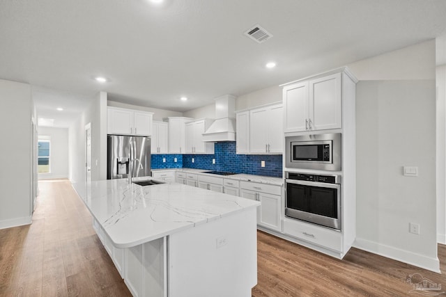 kitchen featuring white cabinets, an island with sink, stainless steel appliances, and custom exhaust hood