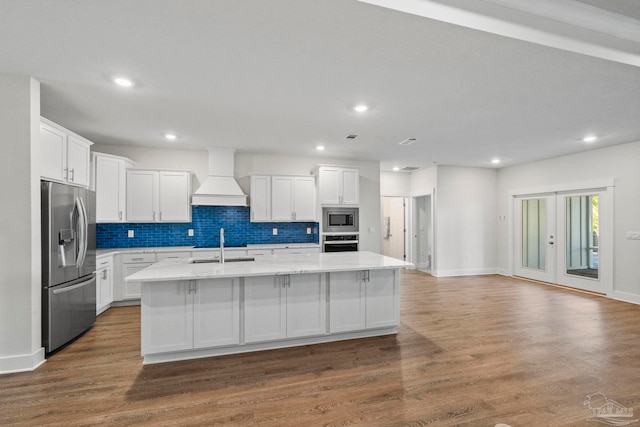 kitchen with hardwood / wood-style flooring, custom range hood, stainless steel appliances, and an island with sink