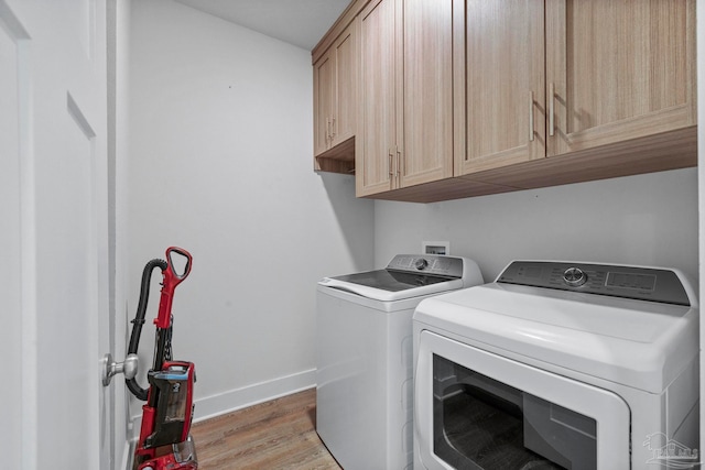 washroom featuring washing machine and clothes dryer, cabinets, and light hardwood / wood-style floors