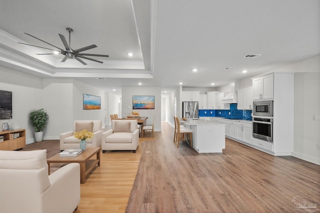 living room with a tray ceiling, light hardwood / wood-style flooring, and ceiling fan