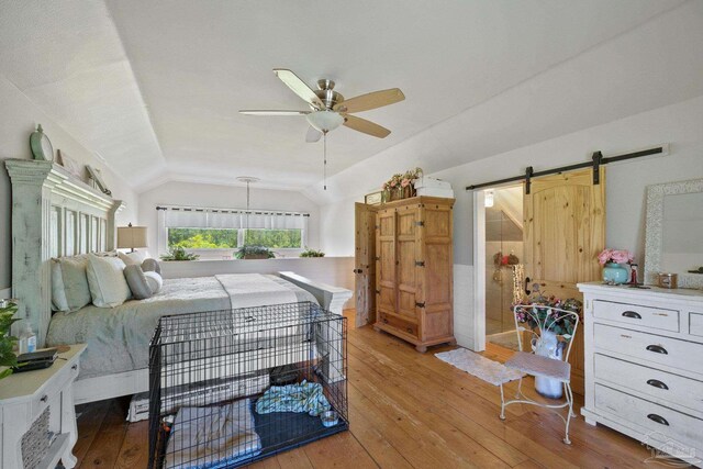 bedroom with vaulted ceiling, a barn door, ceiling fan, and light wood-type flooring