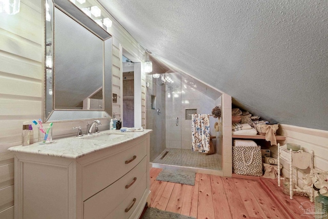 interior space featuring tiled shower, a textured ceiling, vanity, hardwood / wood-style floors, and vaulted ceiling