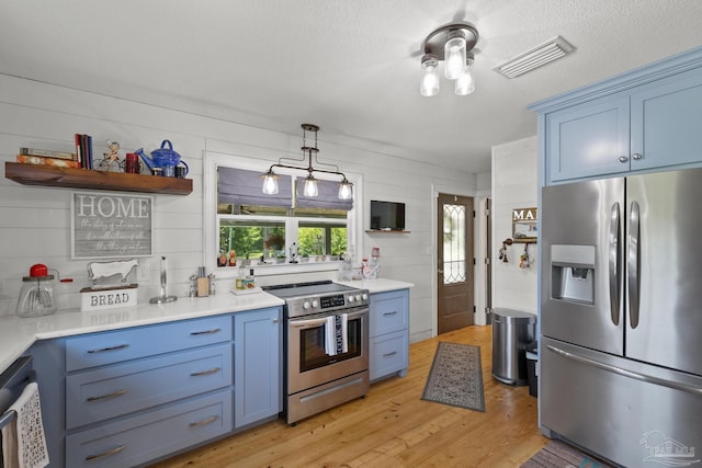 kitchen featuring stainless steel appliances, hanging light fixtures, blue cabinetry, and light hardwood / wood-style floors