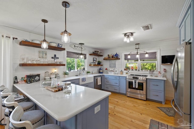 kitchen featuring a breakfast bar area, stainless steel appliances, pendant lighting, kitchen peninsula, and light hardwood / wood-style floors