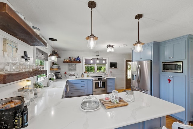 kitchen with kitchen peninsula, appliances with stainless steel finishes, blue cabinetry, wood-type flooring, and decorative light fixtures