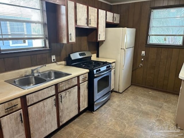 kitchen with sink, gas range, white fridge, and wood walls