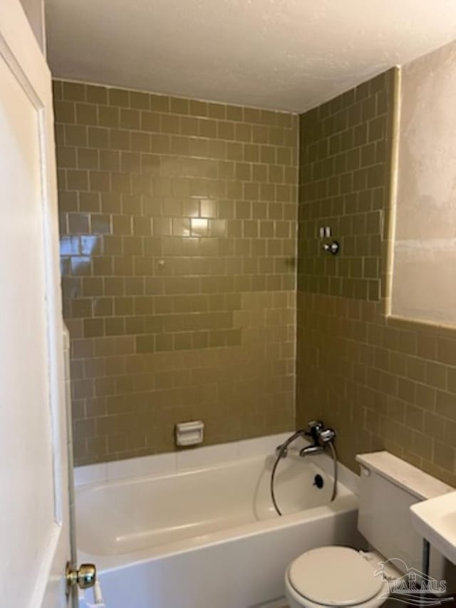 bathroom featuring toilet, tiled shower / bath combo, and a textured ceiling