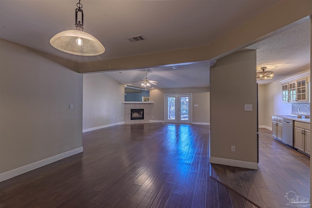 unfurnished living room with french doors, a textured ceiling, ceiling fan, dark wood-type flooring, and a tiled fireplace