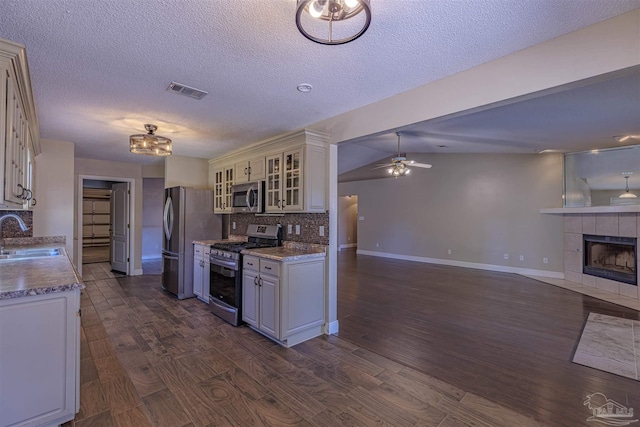 kitchen featuring lofted ceiling, sink, a fireplace, tasteful backsplash, and stainless steel appliances