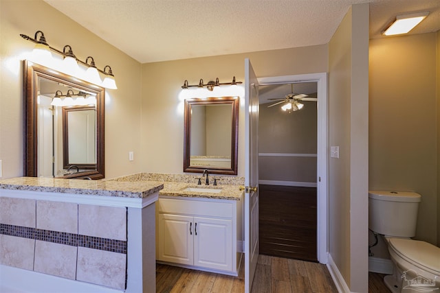 bathroom with hardwood / wood-style floors, vanity, ceiling fan, toilet, and a textured ceiling