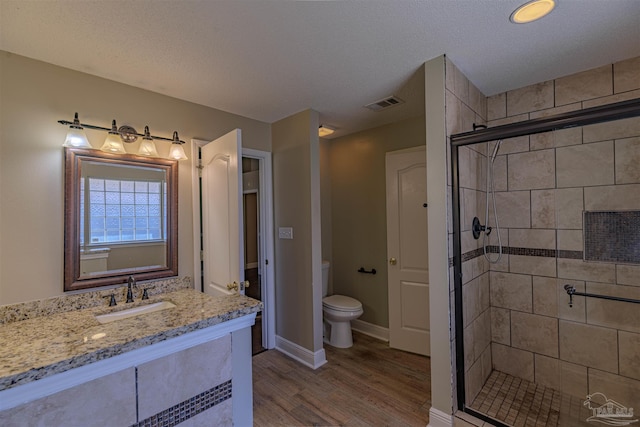 bathroom with vanity, wood-type flooring, toilet, a textured ceiling, and a shower with shower door