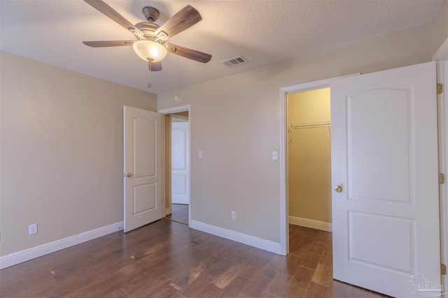 unfurnished bedroom featuring a spacious closet, ceiling fan, dark wood-type flooring, a textured ceiling, and a closet