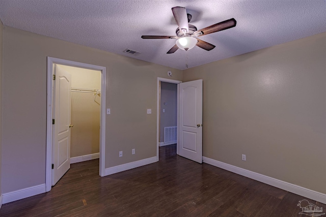 unfurnished bedroom featuring a walk in closet, ceiling fan, a textured ceiling, dark hardwood / wood-style flooring, and a closet