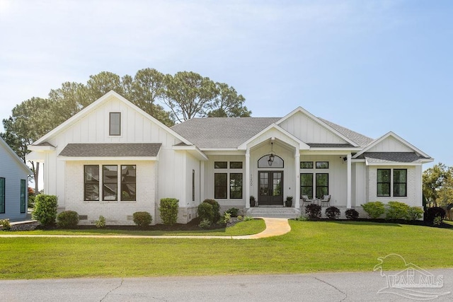 view of front of home featuring board and batten siding, brick siding, a shingled roof, french doors, and a front yard