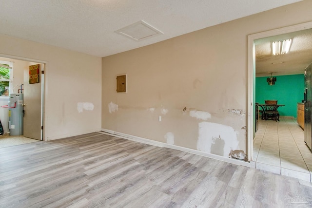 spare room featuring attic access, electric panel, light wood-style flooring, and electric water heater