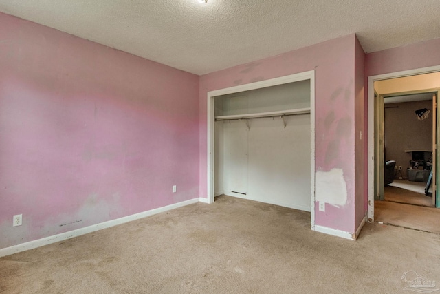 unfurnished bedroom featuring a closet, light colored carpet, a textured ceiling, and baseboards