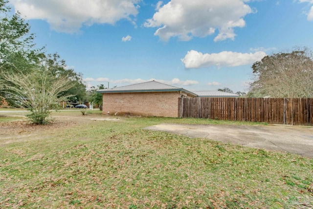 view of property exterior with brick siding, fence, and a lawn