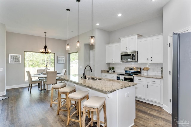 kitchen featuring decorative light fixtures, appliances with stainless steel finishes, a kitchen island with sink, a sink, and white cabinetry