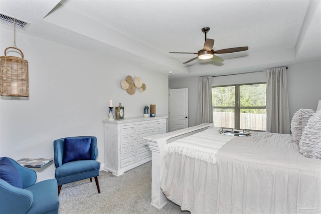 bedroom with light carpet, visible vents, a raised ceiling, and a ceiling fan